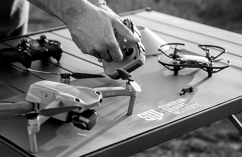SDI presents ASUT drone operations certificates program image of hands and drones on a table with SDI logo. The Sonoran Desert Institute is offering the ASUT educational program.