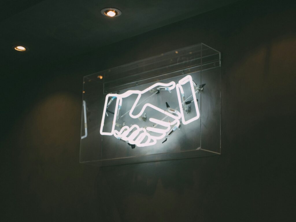 Digital handshake sign as Ernst & Young (EY) has expanded its alliance with SymphonyAI, pushing the partnership into manufacturing and supply chain intelligence.