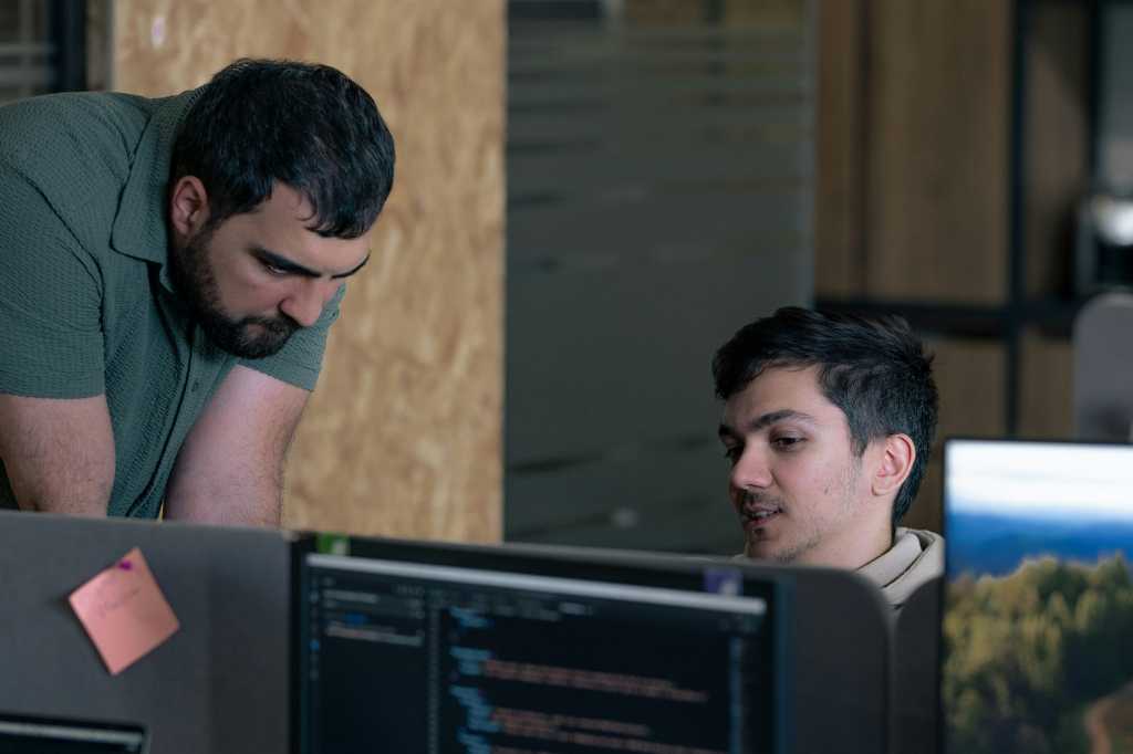 AI Rewrote the Rules of Software Development. Is Cybersecurity Ready for the Next Revolution? Two men working on computers in an office Code inspection with programmers